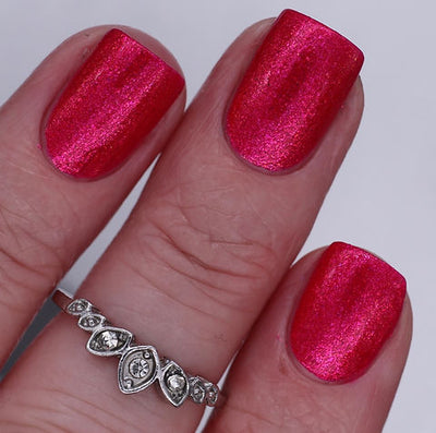 Beach Towel by 'Ard As Nails, vivid magenta-red with warm red-to-pink metallic shimmer shift, on a light skin tone hand
