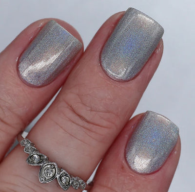Cosmic by 'Ard As Nails, cool silver linear holographic with metallic shimmer in studio light, on a light skin tone hand