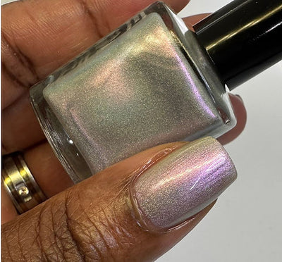 Blushing Bridesmaid by 'Ard As Nails, pink-to-green duochrome shimmer topper revealing full color-shift range in bright daylight, bottle held in a deep skin tone hand