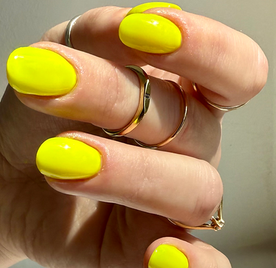 Lightning Speed by 'Ard As Nails, electric neon yellow creme with high-gloss finish, dual-angle swatch under indoor warm lighting, on a light skin tone hand