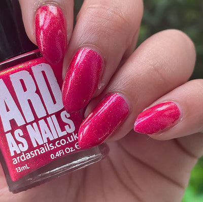 Beach Towel by 'Ard As Nails, raspberry red shimmer with warm golden shimmer particles in bright daylight, bottle held in a light skin tone hand