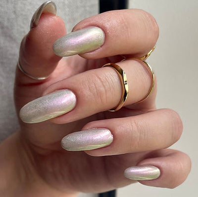 Blushing Bridesmaid by 'Ard As Nails, sheer pearl base with shifting pink-to-green multichrome shimmer topper in studio lighting, on a light-medium skin tone hand
