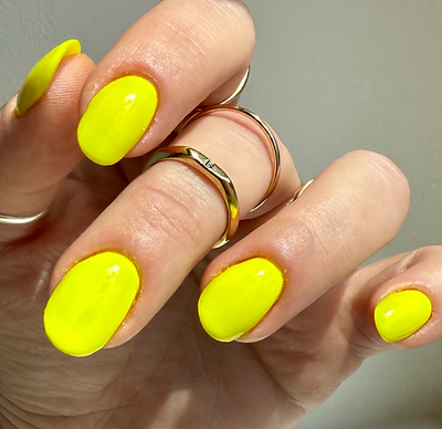 Lightning Speed by 'Ard As Nails, neon yellow creme with glossy reflection in bright daylight, on a light skin tone hand