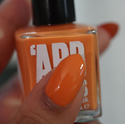 Sunset by 'Ard As Nails, warm orange creme showing bottle and nail swatch, bottle held in a medium-deep hand