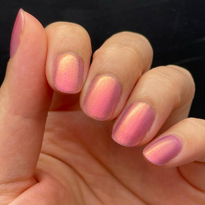 Maui by Dam Nail Polish, sheer rosy pink multichrome shimmer with golden peach shift, on a light skin tone hand