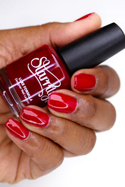 Bloodbelly Jelly by Starrily, bright true red jelly with built-up glossy coverage, bottle held in a deep skin tone hand