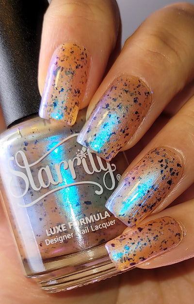 Pi Day Gift Set (Limited Edition) by Starrily, sheer peachy jelly base with navy-to-cyan-to-purple ultrachrome flakie shards showing vivid aurora flash, bottle held in a medium skin tone hand