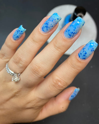 Blueberry Sanctuary by Dam Nail Polish, sheer light blue jelly crelly with assorted cobalt blue metallic glitters and holographic glitter dusting, on a light-medium skin tone hand