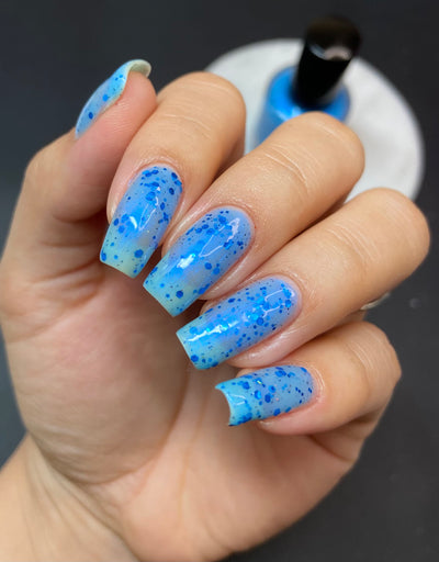 Blueberry Sanctuary by Dam Nail Polish, sheer light blue crelly with blue-to-purple shifting shimmer and assorted cobalt metallic glitter particles, on a light-medium skin tone hand