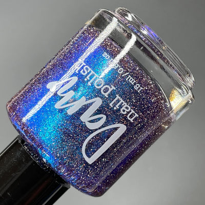 Robots Don't Poop by Dam Nail Polish, blue-purple multichrome shimmer with silver reflective glitter sparkling under direct flash, bottle standalone product shot
