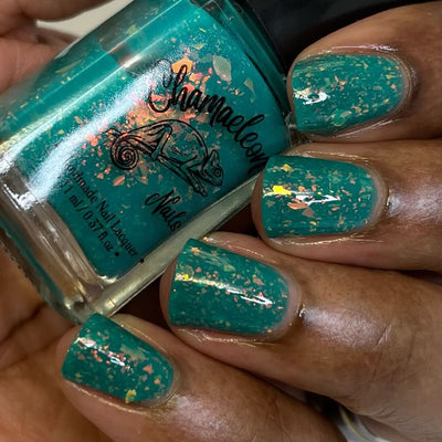Kuang Si Falls by Chamaeleon Nails, teal neon flakie jelly with dense orange-to-yellow iridescent flakes, bottle held in a deep skin tone hand
