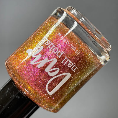 I Like Cheese but I'm Lactose by Dam Nail Polish, muted orange base with orange-to-pink-to-gold multichrome shimmer and silver reflective glitter, bottle standalone product shot