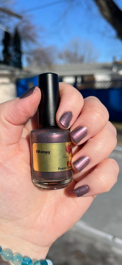 Whimsey by Prairie Crocus Polish, smokey mauve-purple shimmer with rosy pink metallic sheen, bottle held in a light skin tone hand