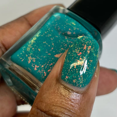 Kuang Si Falls by Chamaeleon Nails, teal neon flakie jelly with orange-to-yellow-green multichrome flake shift, bottle held in a rich skin tone hand
