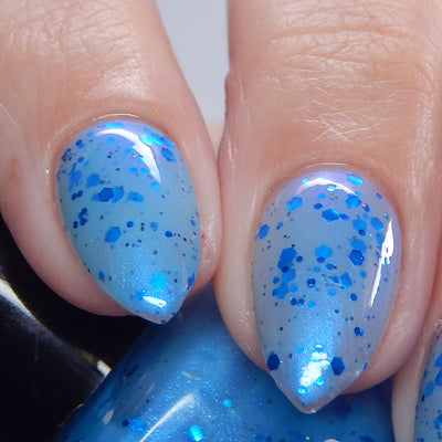 Blueberry Sanctuary by Dam Nail Polish, sheer light blue crelly with mixed-size metallic blue glitters from small dots to large hex chunks and blue-to-purple shifting shimmer, on a light skin tone hand