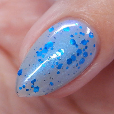 Blueberry Sanctuary by Dam Nail Polish, sheer light blue-grey crelly with metallic blue hex glitters and blue-to-purple color-shifting shimmer, on a light skin tone hand