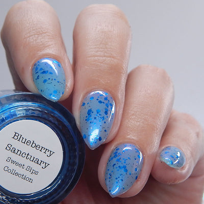 Blueberry Sanctuary by Dam Nail Polish, translucent light blue holographic shimmer crelly with scattered metallic blue glitters in varied sizes and blue-purple shifting shimmer, on a light skin tone hand
