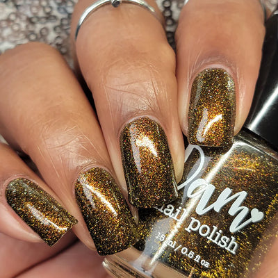 Champagne Sparkles by Dam Nail Polish, deep black-brown jelly with bronze-gold shimmer and holographic-scatter reflective glitter under indoor warm light, on a light-medium skin tone hand
