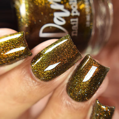 Champagne Sparkles by Dam Nail Polish, black jelly with bronze-gold shimmer and gold reflective glitter illuminated under direct flash, on a light-medium skin tone hand