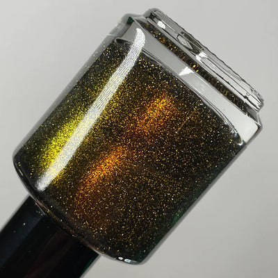 Champagne Sparkles by Dam Nail Polish, black jelly base with amber-gold shimmer and gold reflective glitter showing a yellow-green edge shift under studio light, bottle standalone product shot