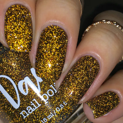 Champagne Sparkles by Dam Nail Polish, deep black-brown jelly with warm amber-gold microglitter and bronze shimmer reading rich gold under indoor warm light, on a light skin tone hand