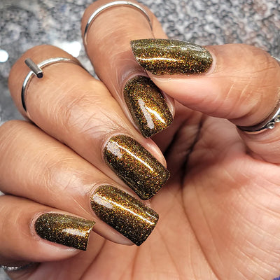 Champagne Sparkles by Dam Nail Polish, near-black jelly with bronze-gold shimmer and linear holographic reflective glitter sparks in bright daylight, on a light-medium skin tone hand
