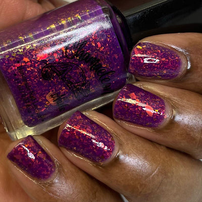 Evening in Provence by Chamaeleon Nails, magenta jelly with dense orange-red and gold multichrome flakies showing glassy finish under flash, bottle held in a deep hand