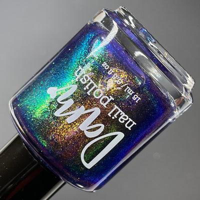 Sandman by Dam Nail Polish, deep blurple jelly with densely packed gold, green, and blue color-shifting shimmer particles, bottle standalone product shot