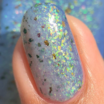 The Forgotten Lagoon (UV Polish) by Chamaeleon Nails, soft lavender-white flakie UV with dense green-to-gold iridescent and bronze UCC flakes in bright daylight UV activation, on a light skin tone hand