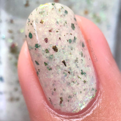 The Forgotten Lagoon (UV Polish) by Chamaeleon Nails, milky white crelly flakie UV in resting state with green UCC flakes and bronze ultrachrome shards under indoor warm light, on a light skin tone hand