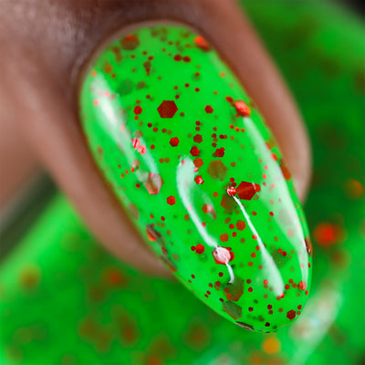 Light the Flame by Cadillacquer, macro close-up of neon green base with multi-sized red and orange-red metallic hex glitter particles