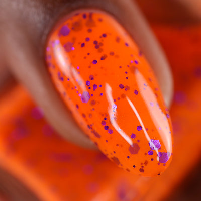 Endure And Survive by Cadillacquer, macro close-up of dense multi-size metallic purple hex glitter across a vivid neon orange base