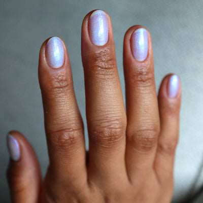 The Fire's Burning Blue by Cadillacquer, soft lavender-periwinkle shimmer with blue-violet iridescent shift across five nails, on a medium-deep skin tone hand