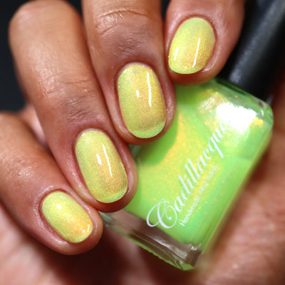 The Last Ray of Dying Light by Cadillacquer, soft yellow shimmer glow-in-the-dark with warm orange-gold shimmer shift, bottle held in a medium hand