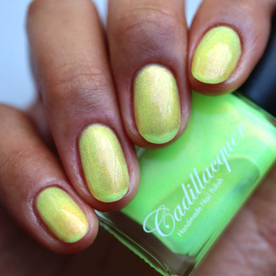 The Last Ray of Dying Light by Cadillacquer, soft yellow base with strong red-orange shimmer shift, bottle held in a medium-deep hand