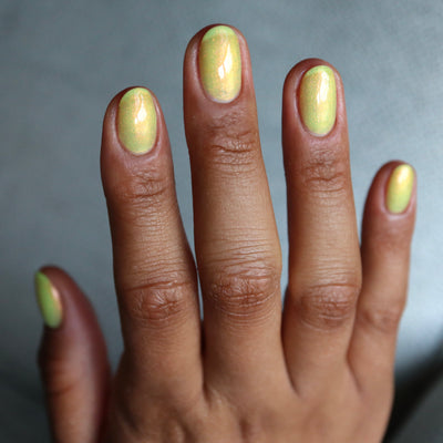 The Last Ray of Dying Light by Cadillacquer, soft yellow-green base with vivid red-to-orange shimmer shift across nail surface, on a medium-deep skin tone hand