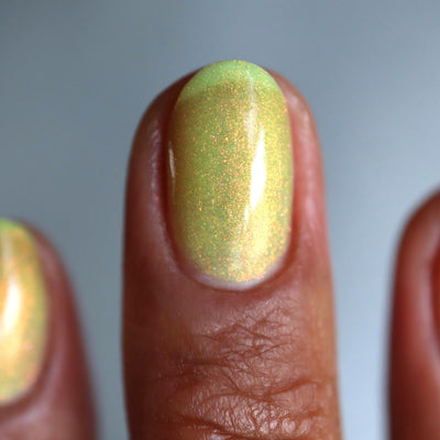 The Last Ray of Dying Light by Cadillacquer, yellow shimmer glow-in-the-dark showing red-orange flash shifting to golden in direct light, on a deep skin tone hand