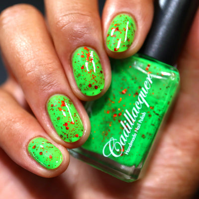 Light the Flame by Cadillacquer, neon lime green jelly glitter glow-in-the-dark with red metallic glitter, bottle held in a medium hand