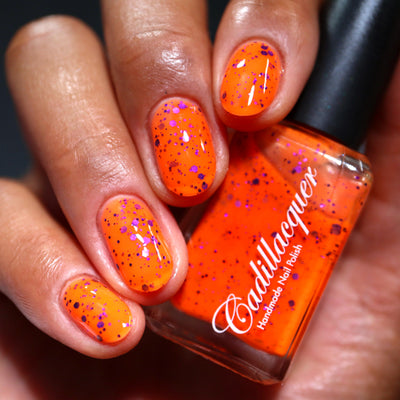Endure And Survive by Cadillacquer, neon orange jelly glitter showing metallic magenta-purple and dark purple glitter of mixed sizes, bottle held in a medium hand