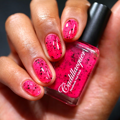 The Night's a Brighter Shade by Cadillacquer, neon hot pink jelly with scattered matte black glitter, bottle held in a medium hand