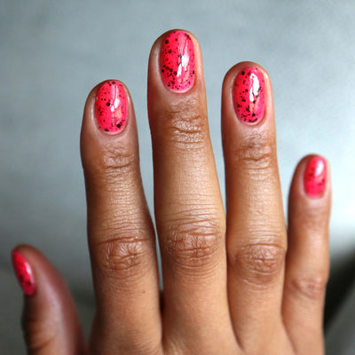 The Night's a Brighter Shade by Cadillacquer, bright hot pink with densely scattered matte black glitter in daylight, on a medium-deep skin tone hand