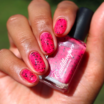 The Night's a Brighter Shade by Cadillacquer, neon hot pink crelly with matte black glitter in bright daylight, bottle held in a medium hand