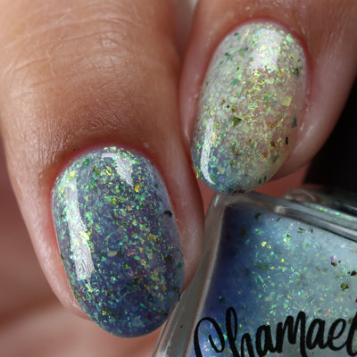 The Forgotten Lagoon (UV Polish) by Chamaeleon Nails, flakie UV layering demo showing slate blue UV-activated nail beside white-grey resting state nail, with green-to-gold iridescent flake shift, layering demo