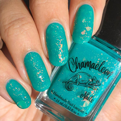 Kuang Si Falls by Chamaeleon Nails, neon teal flakie jelly with orange-gold and yellow-green rainbow flakie flash in daylight, bottle held in a light skin tone hand