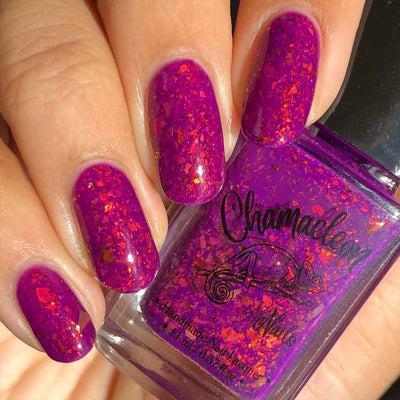 Evening in Provence by Chamaeleon Nails, violet-magenta jelly with orange-red and copper-gold multichrome flakies shifting toward red in bright daylight, on a light skin tone hand