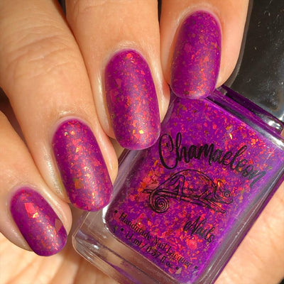 Evening in Provence by Chamaeleon Nails, deep magenta-purple jelly with orange-red and copper-gold flakies shifting to green, bottle held in a light hand