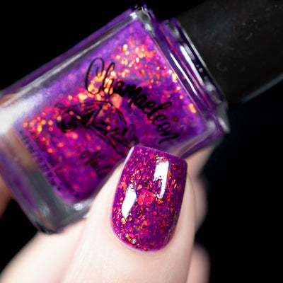 Evening in Provence by Chamaeleon Nails, vivid magenta jelly with red-orange and gold multichrome flakies under direct flash against dark background, bottle held in a light hand