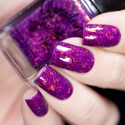 Evening in Provence by Chamaeleon Nails, magenta jelly with high-shine orange-red and copper-gold multichrome flakies under studio light, bottle held in a light hand