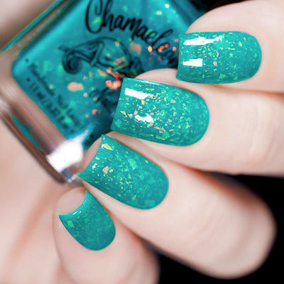 Kuang Si Falls by Chamaeleon Nails, translucent neon teal jelly with scattered orange and yellow-gold iridescent flakies, on a light skin tone hand