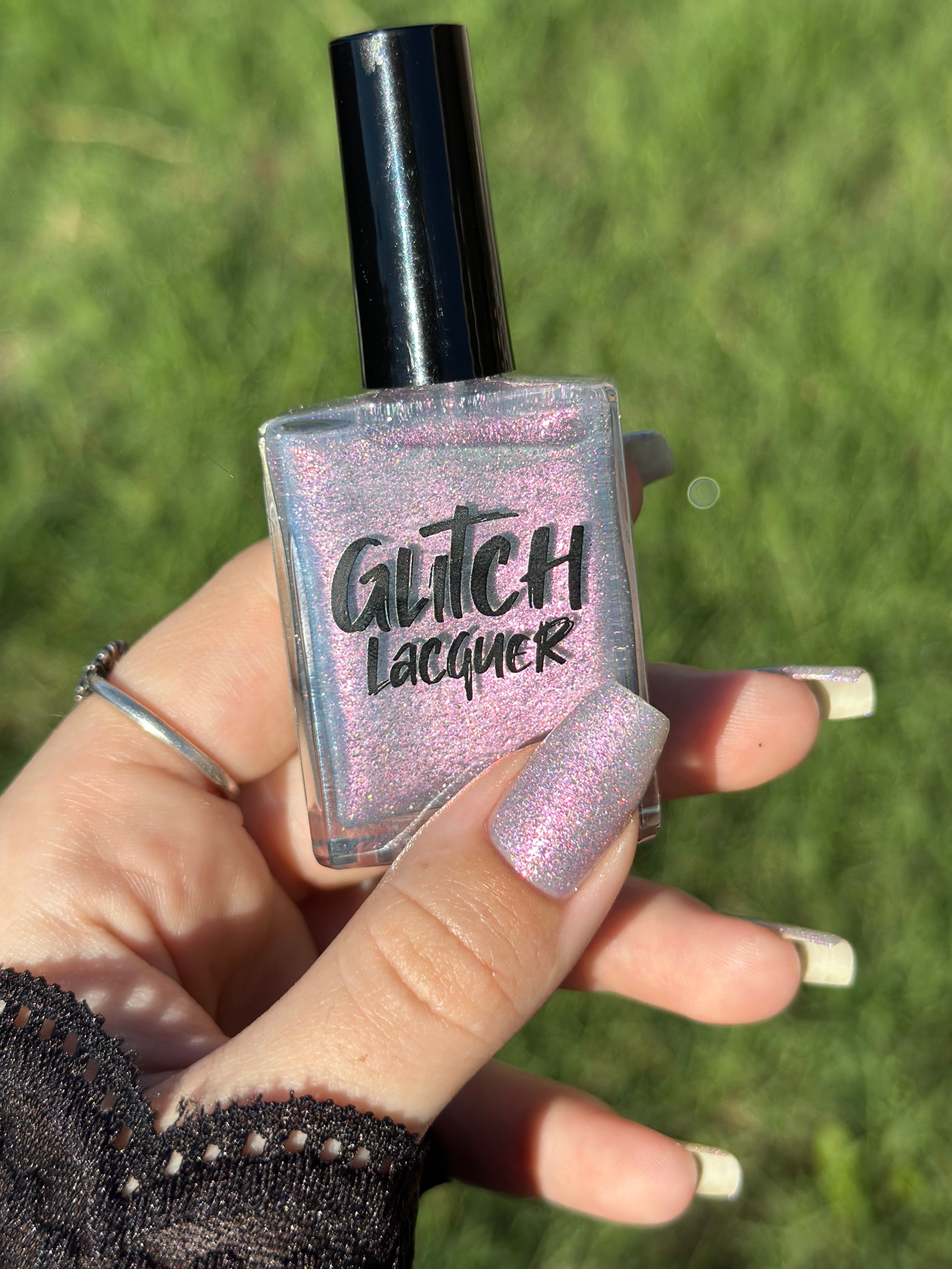 Lavender Haze by Glitch Lacquer on five long coffin nails, very light purple polish with strong pink multichrome shift and sparkly red reflective glitters, light skin tone, bright daylight.